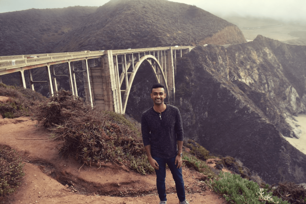 The author on a hike, standing in front of a bridge.